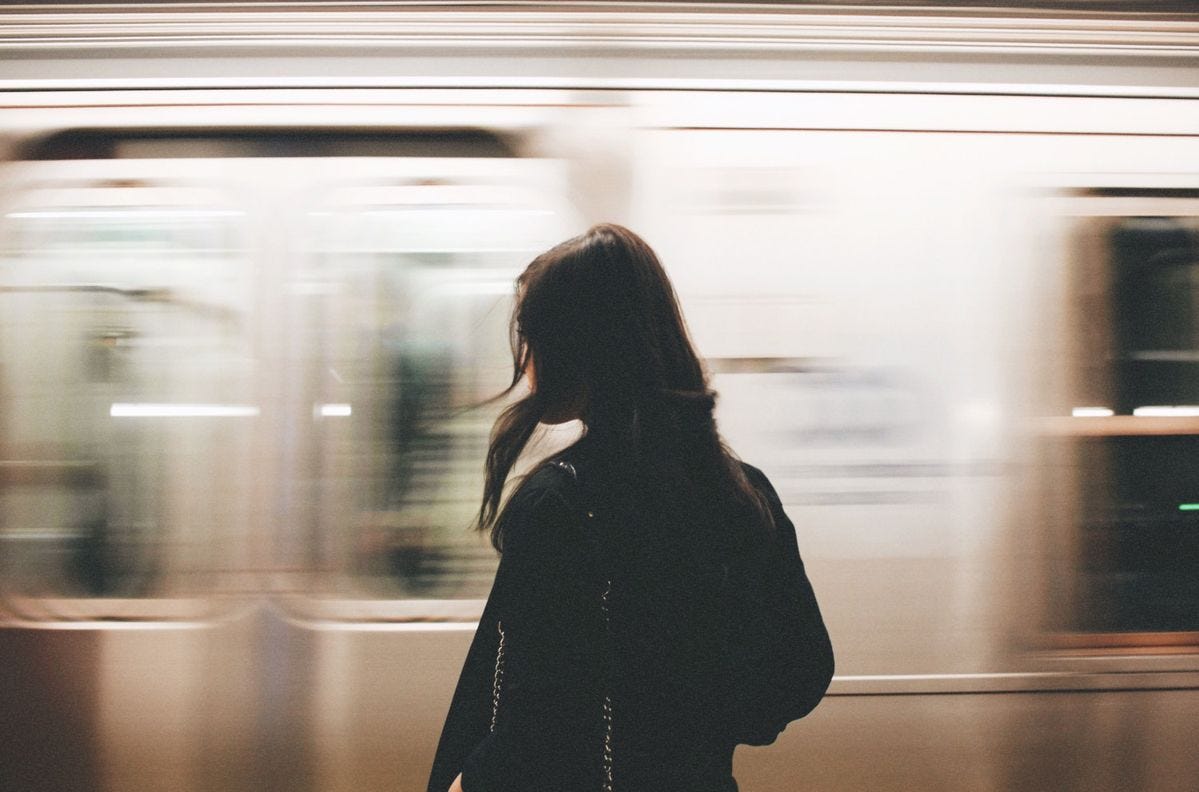 Une jeune femme se tient devant un métro qui passe, avec l'effet de rapidité qui fait un joli flou.