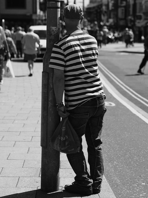 A man on a busy public sidewalk leaning on a lamppost for support. A man on a busy public sidewalk leaning on a lamppost for support.