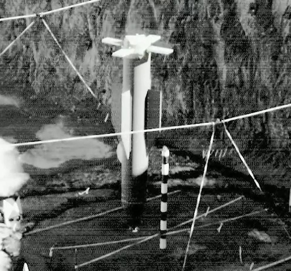 Black and white photo of a rocket-shaped object secured by wires.