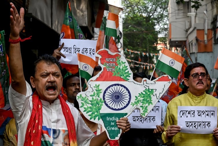 Men march down the street holding replica maps of India with the Indian flag on them. Men march down the street holding replica maps of India with the Indian flag on them.
