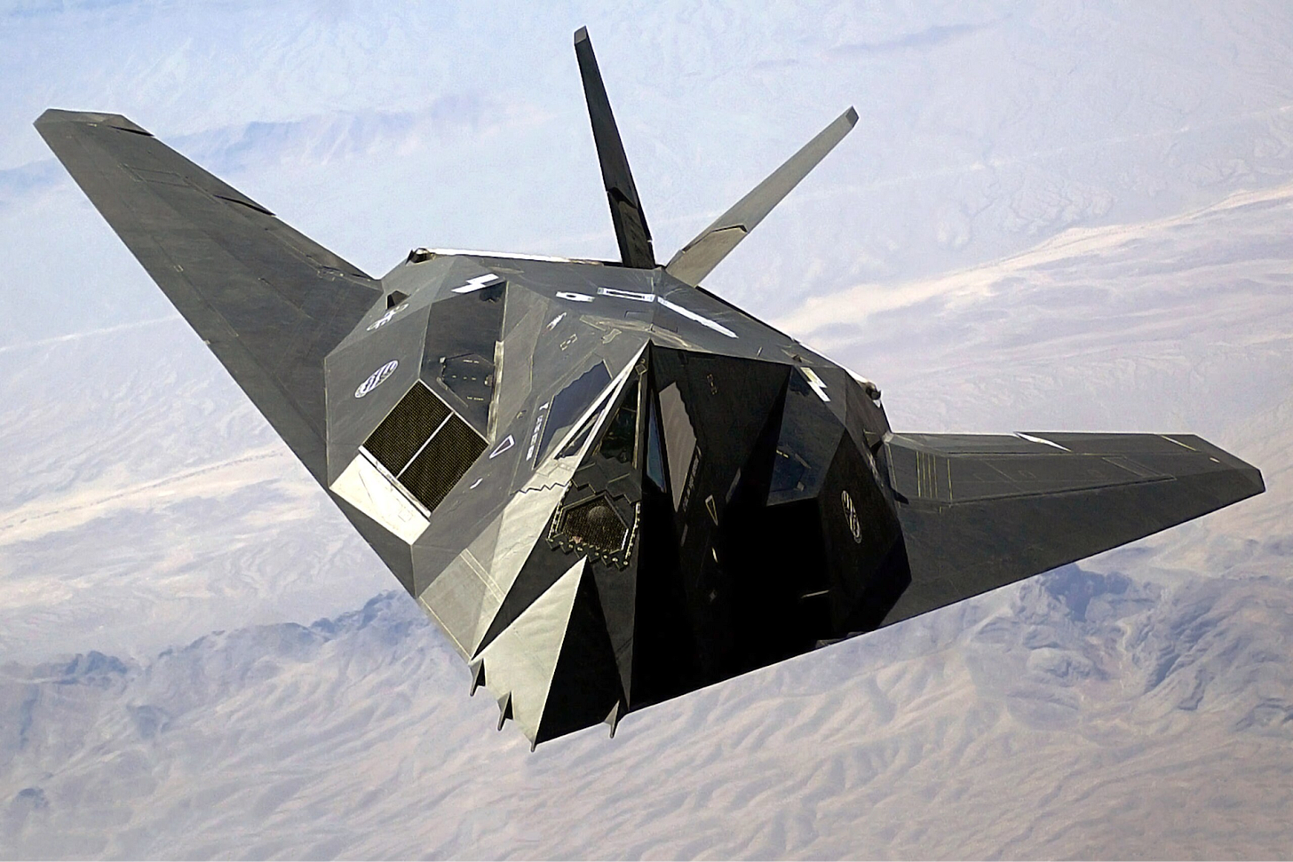 Stealth fighter aircraft flying above desert terrain with open weapons bay.