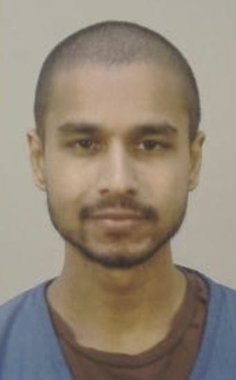 A booking photo taken at the Dane County Jail. The subject has a shaved head and facial hair, wearing a blue jail-issued top, photographed against a plain gray background.