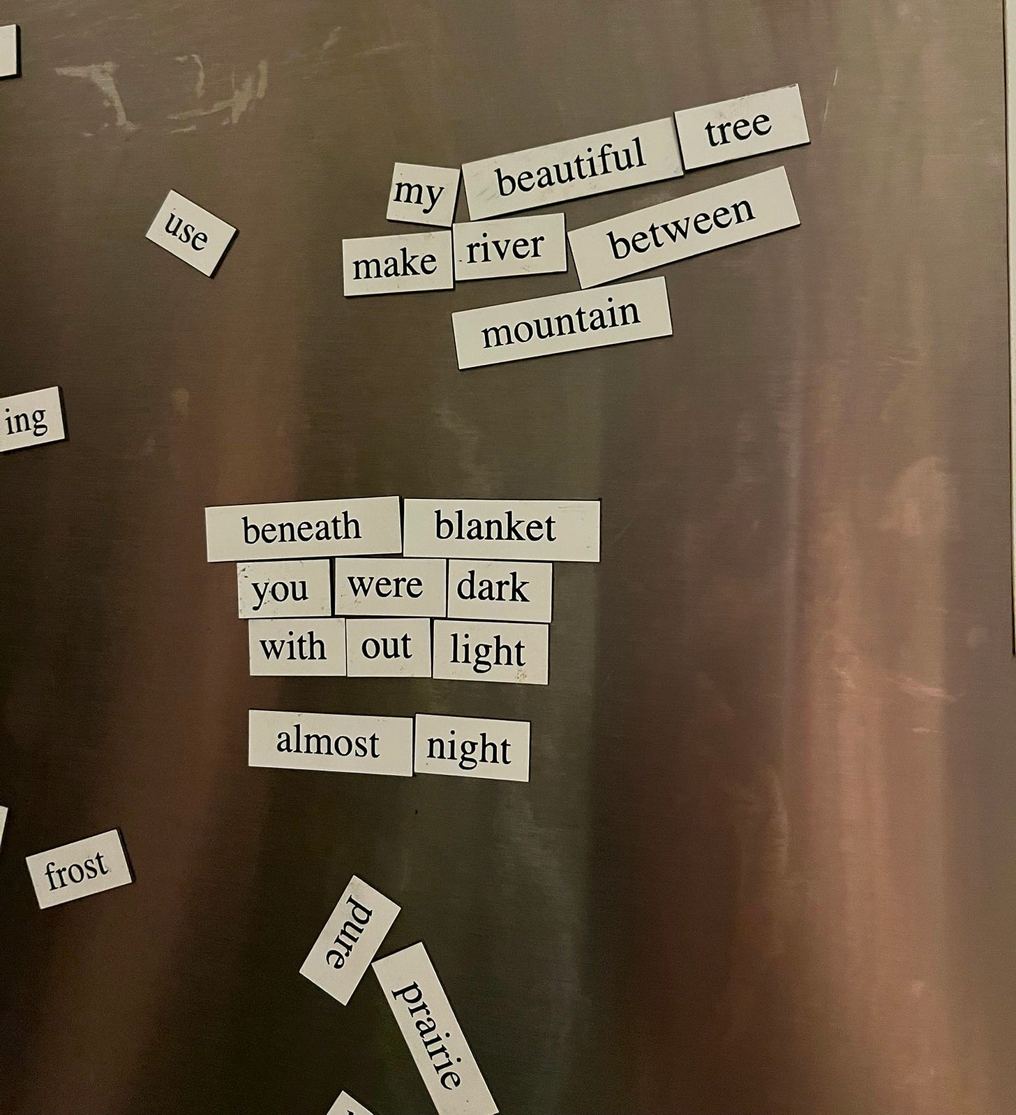 Fridge poem magnets. First poem: "my beautiful tree / make river between / mountain". Second poem: "beneath blanket / you were dark / with out light / almost night".