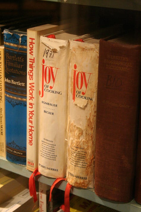 The cover of the first edition of Joy of Cooking, showing a stylized image of St. Martha of Bethany; copies of antique-looking cookbooks, and a stack of cookbooks on a dining room table