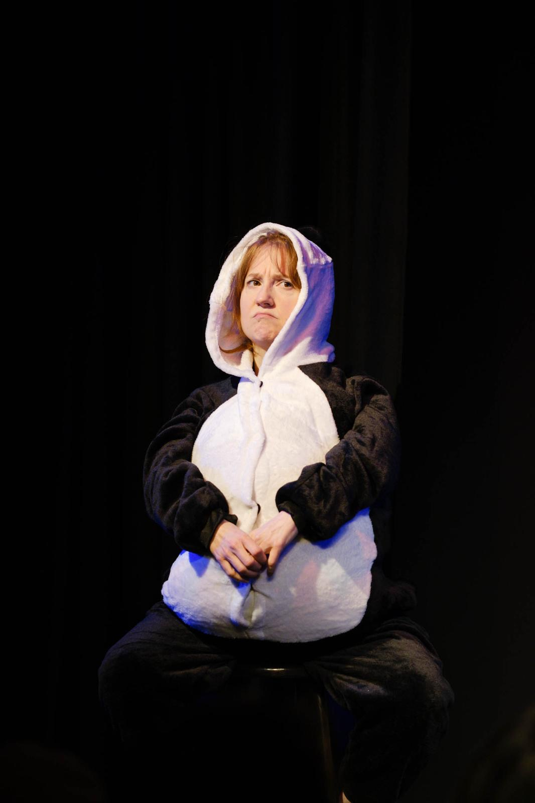 woman dressed as a panda sits on a stool and looks grumpy