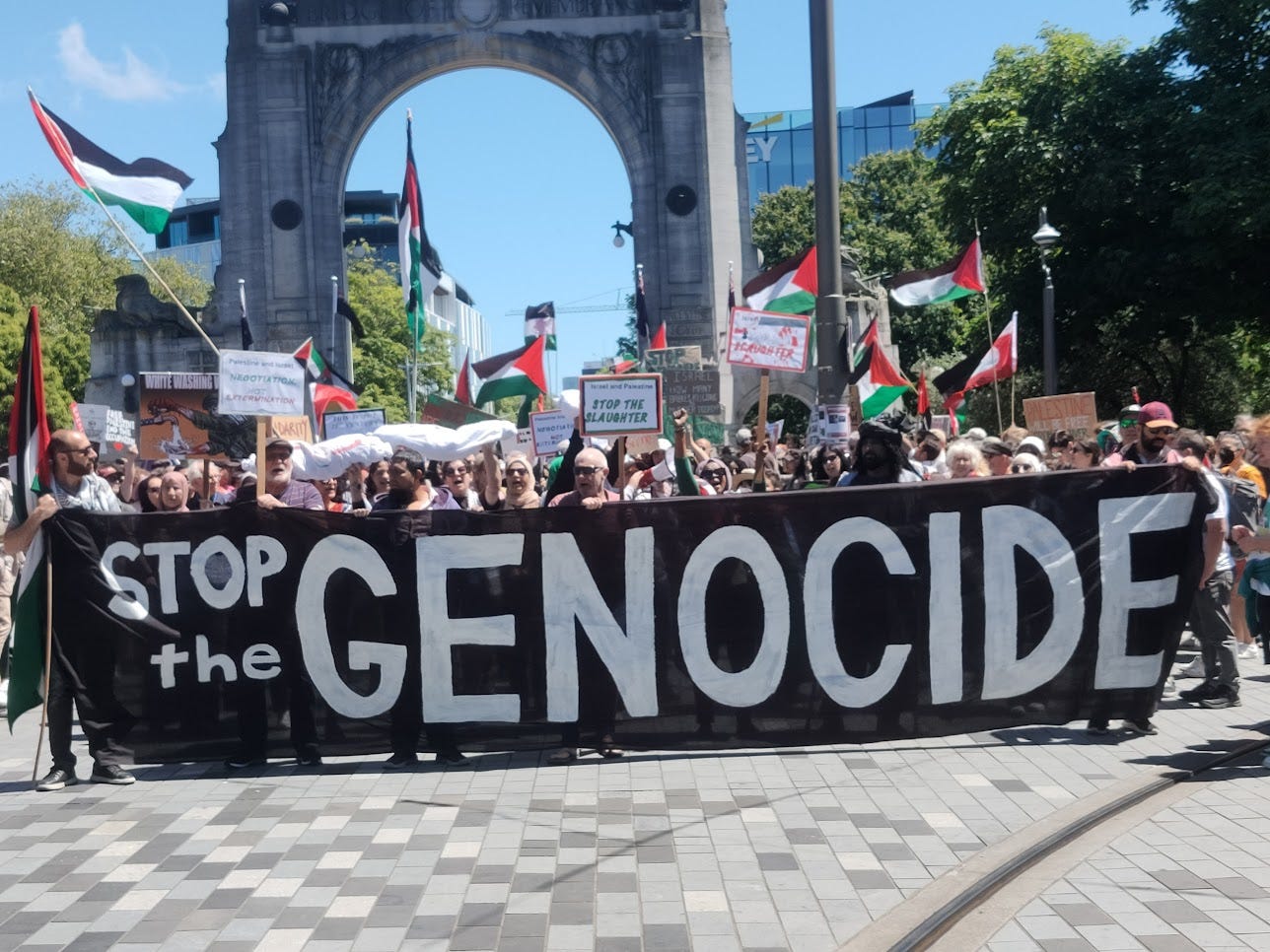 protesters hold a banner reading "Stop the Genocide"