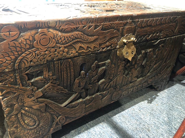 A dark-stained wooden chest ornately carved with images of plants, people, designs and various scenes.