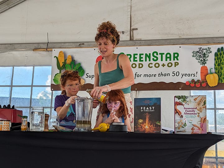 Chef Emma Frisch on stage demonstrating how to make a recipe for Golden Tahini Dressing with her daughters.