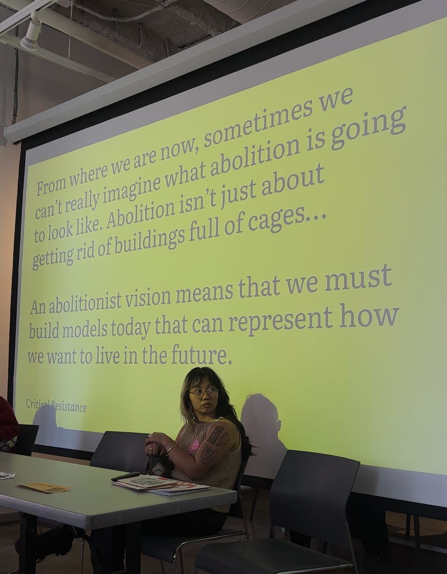 image of MJ sitting in front of a yellow slide with text on it (a quote about Abolition by Ruth Wilson Gilmore) image of MJ sitting in front of a yellow slide with text on it (a quote about Abolition by Ruth Wilson Gilmore)
