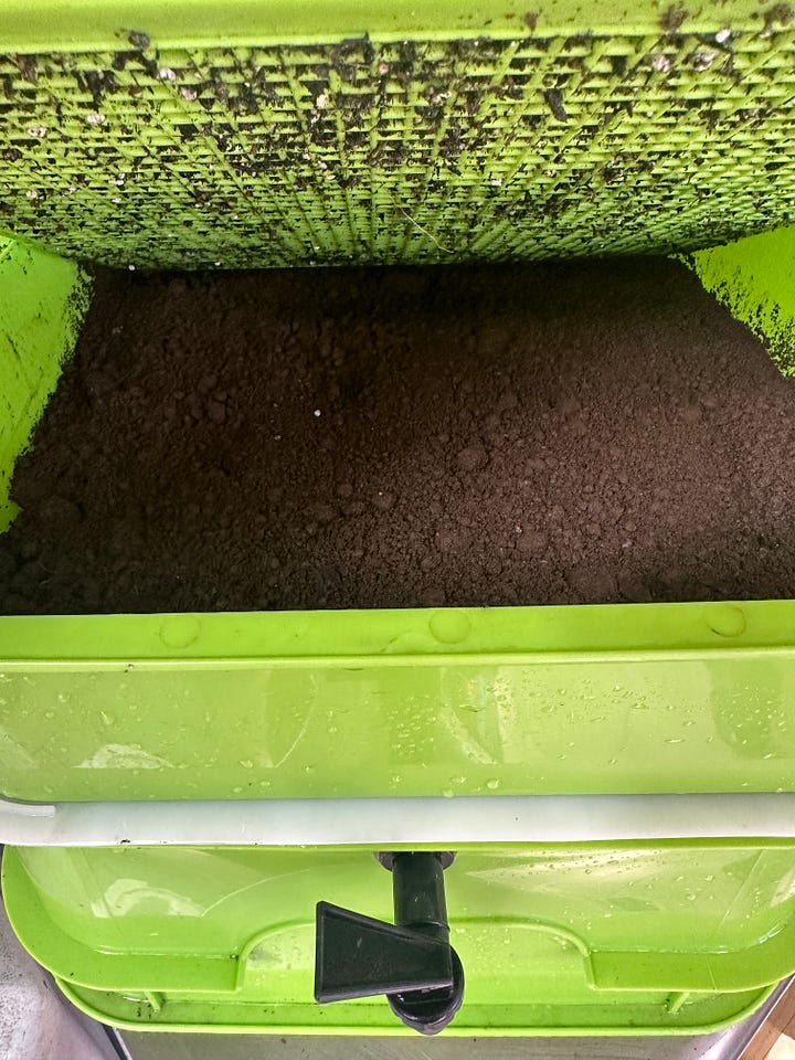 A green multi-layer vermicomposting bin with a black spout.