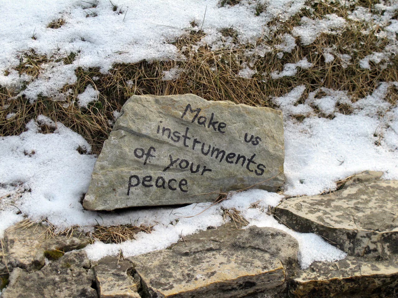 A stone memorial with the inscription 'Make us instruments of your peace' lying on snow-covered ground at Auschwitz-Birkenau concentration camp.