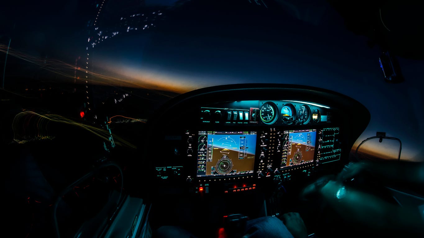 A small aircraft cockpit at dusk, the instrument panel lit against a darkening sky