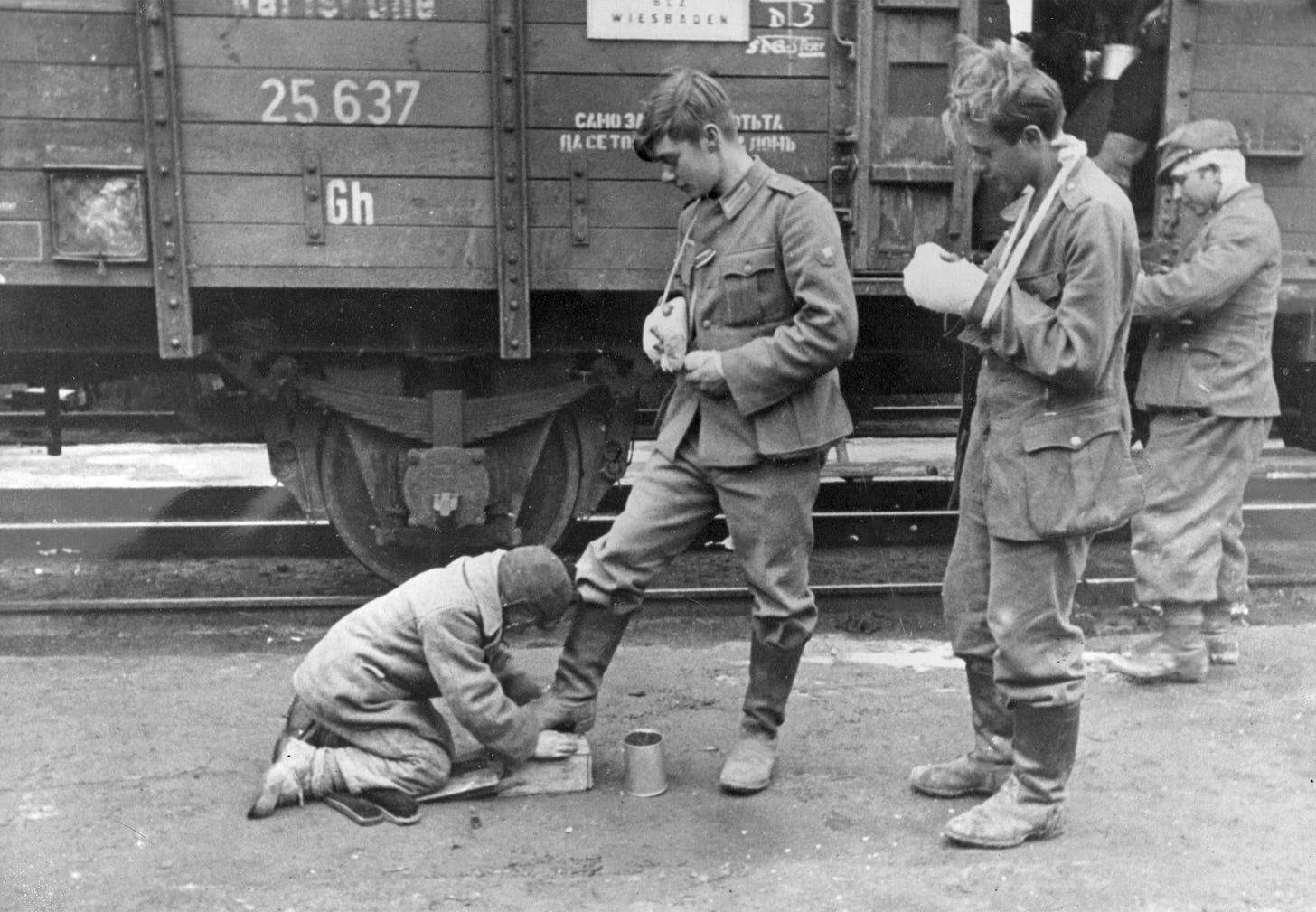 A poignant scene: a Soviet teenager cleans the boots of a wounded German soldier at a train station, 1943.