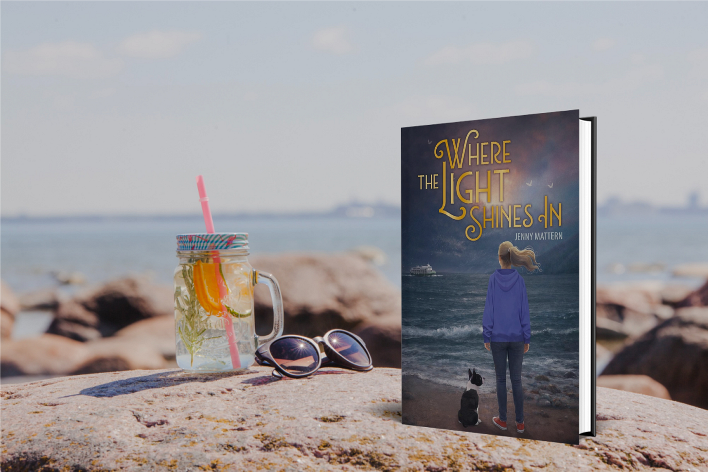 Book "where the Light Shines In" on a rock by the ocean next to a drink and sunglasses
