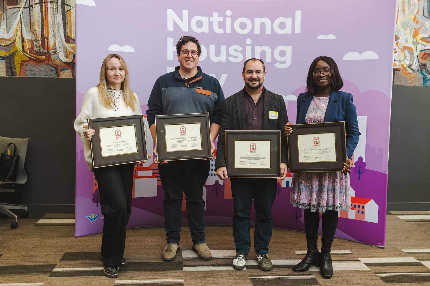 2025 Newcomer Landlord Awards recipients. Four people stading up in front of the National Housing Day banner holding their certificates
