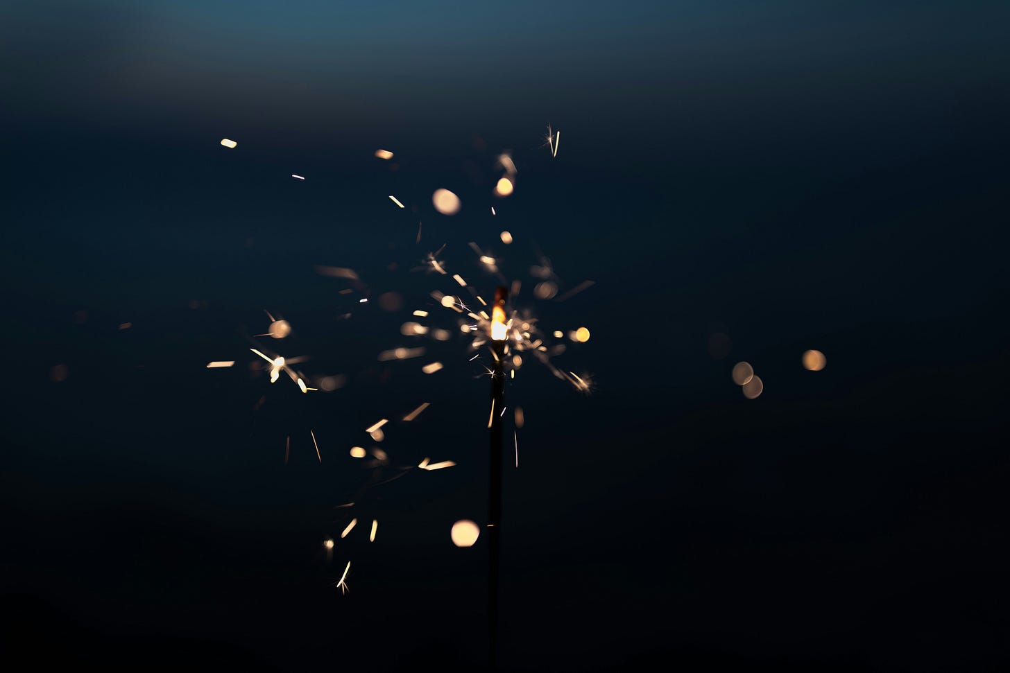 A sparkler flickers yellow and white against a dark background.