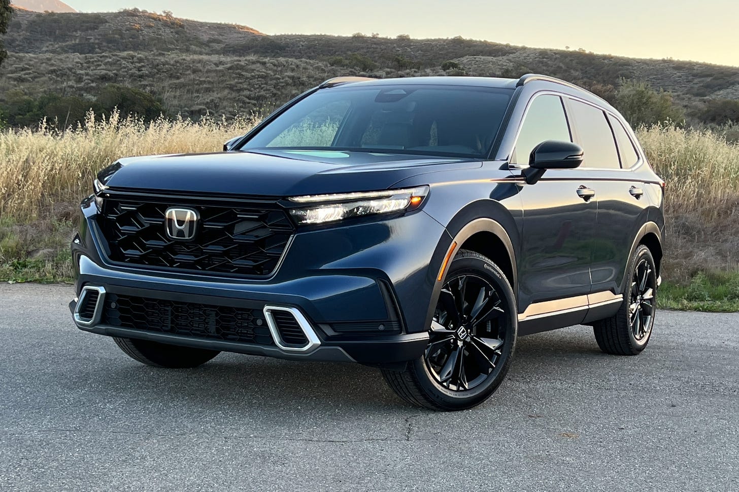 Front-quarter view of a dark blue 2024 Honda CR-V parked near some mountains at sunset.