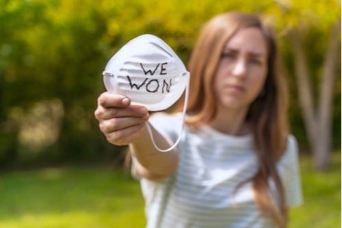 A woman holding up a face mask with the words “WE WON” written on it A woman holding up a face mask with the words “WE WON” written on it