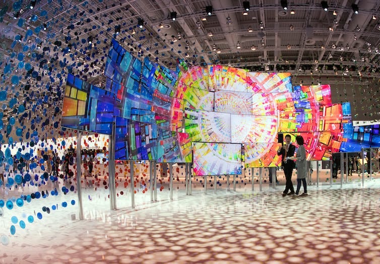 people walk past colorful multi-screen display at a trade show people walk past colorful multi-screen display at a trade show