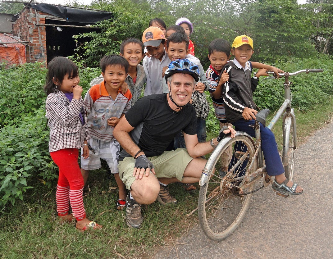 Group of several children in Vietnam smiling for the camera, one is sitting on a large bicycle. A man is crouched down with the kids smiling into the camera and holding onto the rear wheel of the bike. Group of several children in Vietnam smiling for the camera, one is sitting on a large bicycle. A man is crouched down with the kids smiling into the camera and holding onto the rear wheel of the bike.