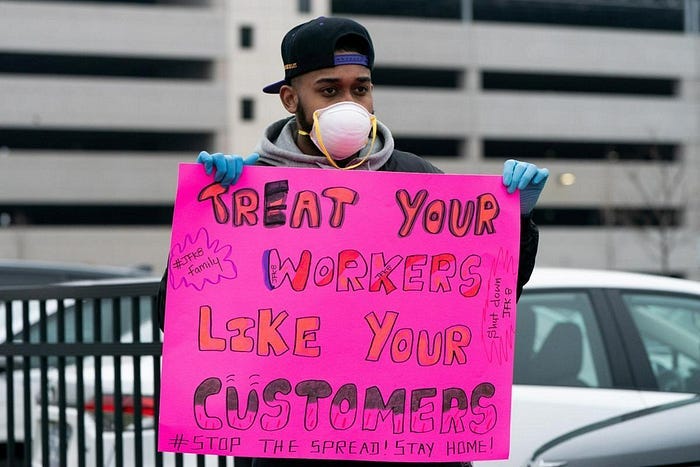 A man in a COVID mask holding up a protest sign saying: treat your workers like your customers A man in a COVID mask holding up a protest sign saying: treat your workers like your customers