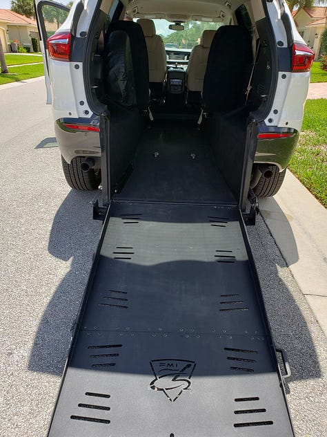 There are 3 photos in a gallery. From left to right: the first photo is the back of a white SUV, but it has been modified and is higher off the ground than normal; the trunk is open, and a wheelchair ramp extends out the back onto the ground. In the second, a red SUV similar to the first in that it has been modified; this view shows the interior of the back, with a built-in wheelchair ramp. The third is a picture of the writer of this piece; she is standing in a driveway with a walker, wearing a burgundy cardigan, black tank top, jeans, one sneaker, and one boot on her feet; behind her is a Silver 2023 Honda Odyssey minivan.