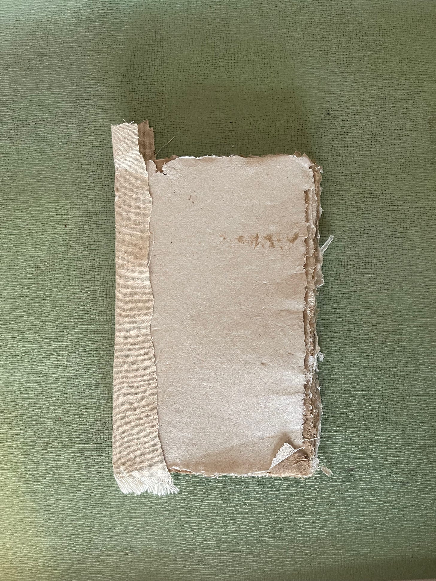 A paper block of folded signatures, handsewn, and bound with glue and fabric on a green background A paper block of folded signatures, handsewn, and bound with glue and fabric on a green background