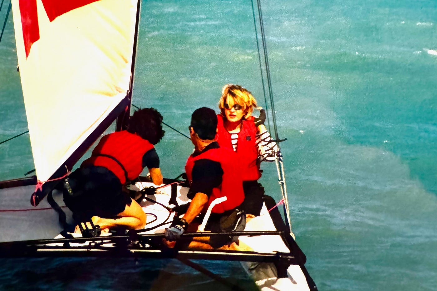 Two men and a woman wearing red life vests on a hobie cat sailboat