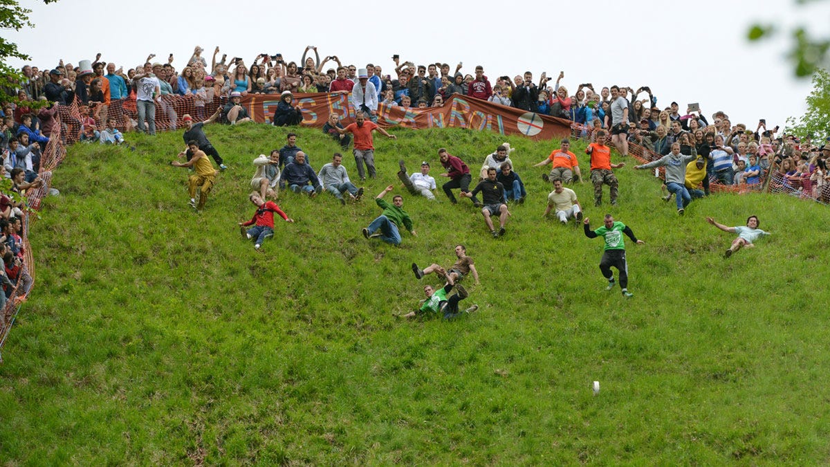 A crowd of people at the top of a hill watching a small group run down the hill A crowd of people at the top of a hill watching a small group run down the hill