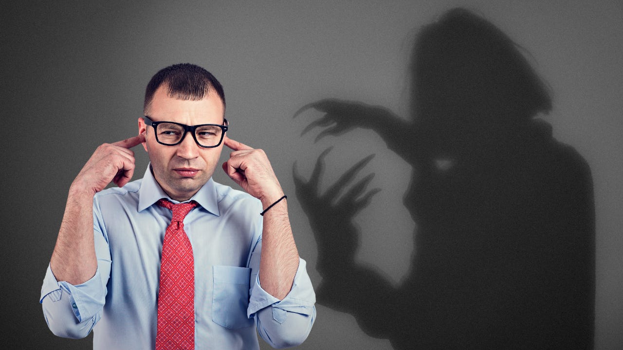 A devilish shadow behind a man with his fingers in his ears.