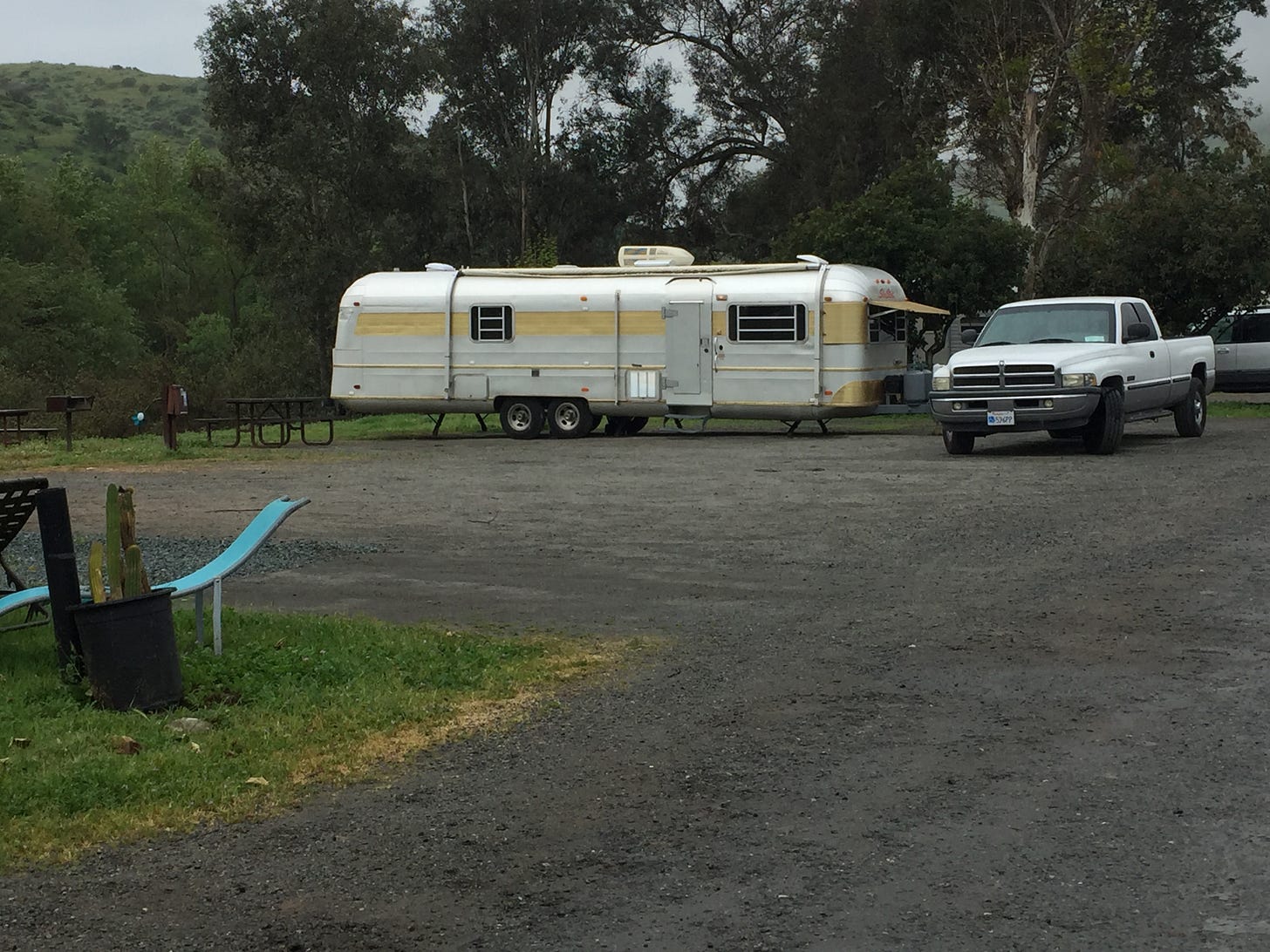 Aluminum Silver Streak Trailer with a White Dodge Truck parked in a campsite in Southern California on a cloudy grey day after the rain.