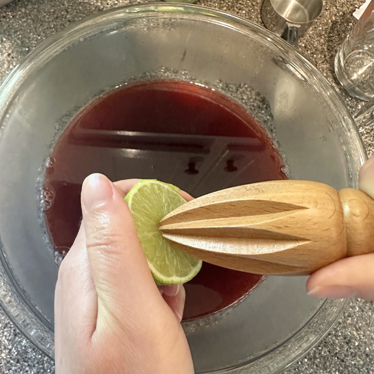 Juicing a lime over a bowl of hibiscus tea using a wood citrus juicer