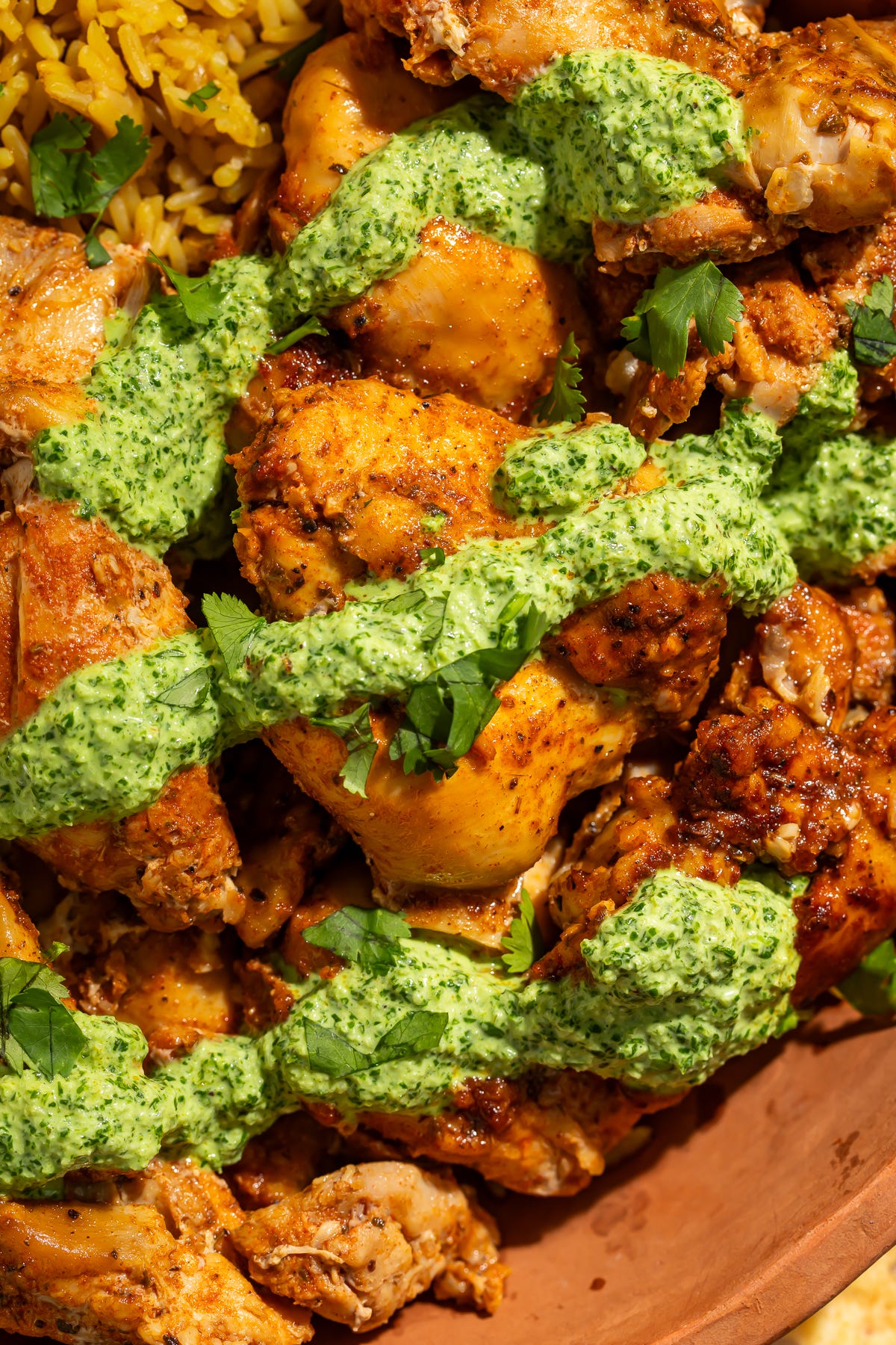 Close up of a terra cotta bowl filled with yellow rice, topped with slow cooker Peruvian chicken and drizzled with aji verde (green sauce)