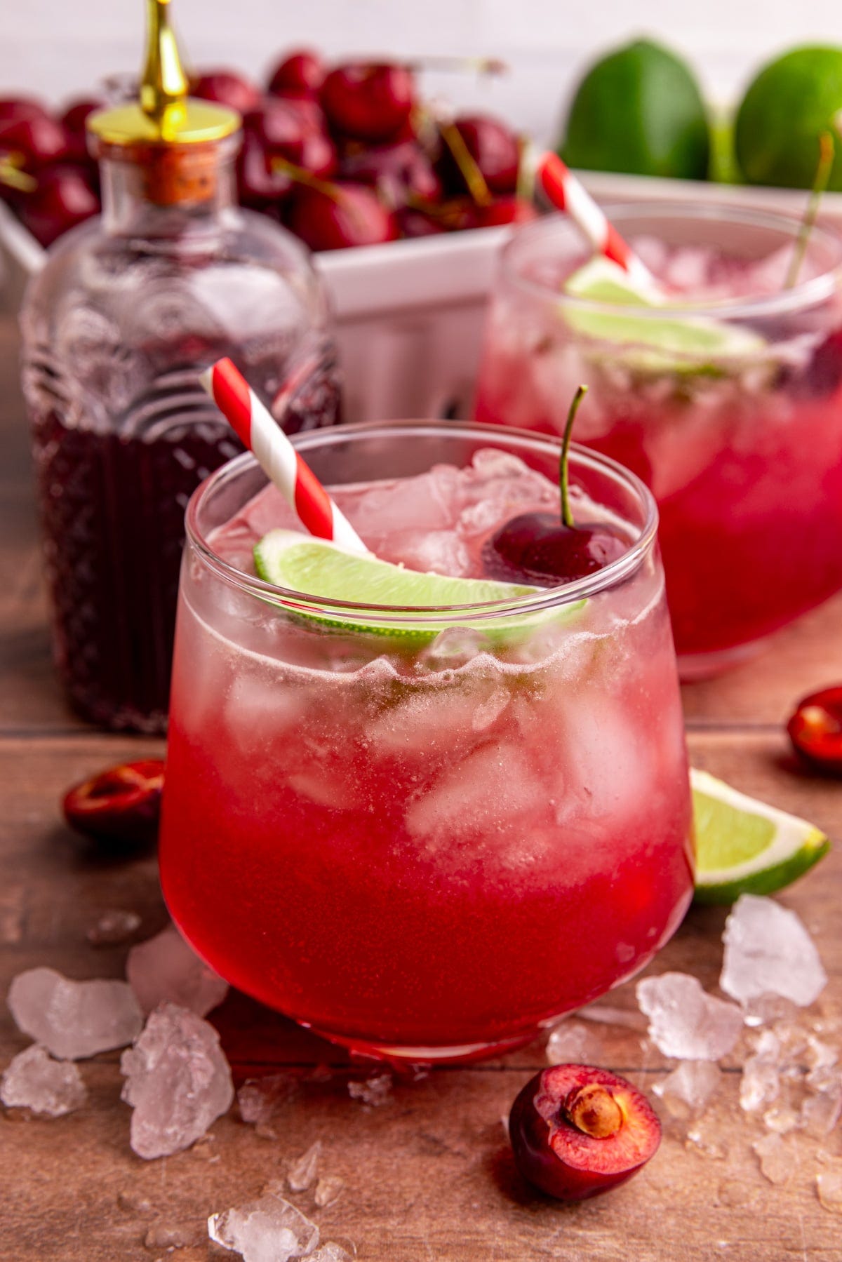A cherry mocktail, on a table with ice, garnished with a lime wedge and a cherry.