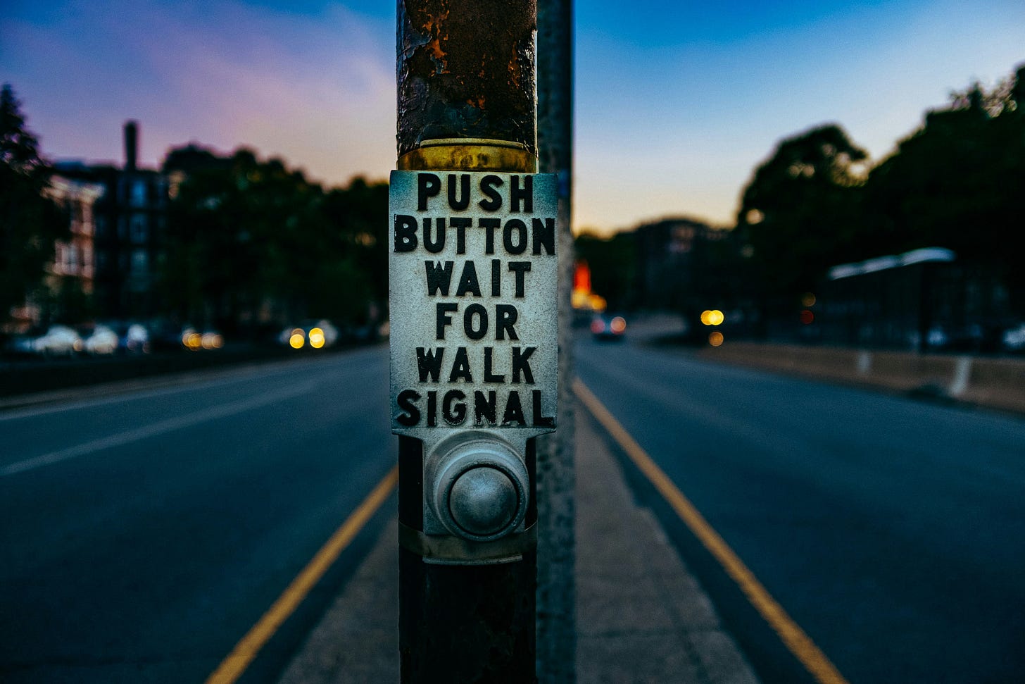 Pedestrian crossing button at dusk with a sign reading “PUSH BUTTON WAIT FOR WALK SIGNAL. Pedestrian crossing button at dusk with a sign reading “PUSH BUTTON WAIT FOR WALK SIGNAL.