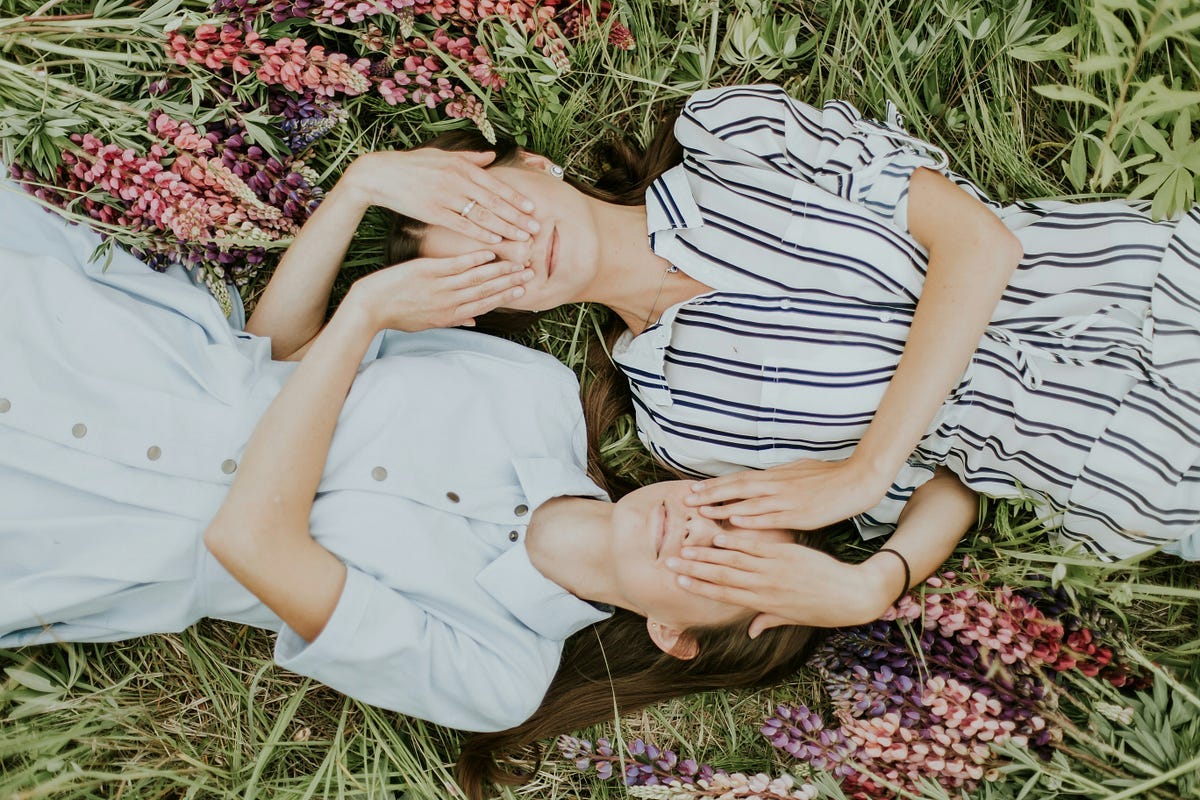 twins covering faces lying on grass