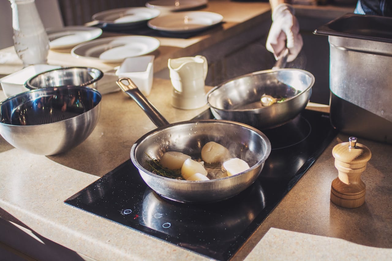 Stock photo of pans (with food) on a two burner induction stove with bowls and plates in the background. Obviously not my kitchen because it is clean and the food looks edible.
