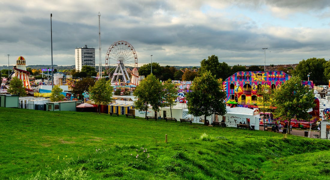 A wide shot of Goose Fair funfair with rides, stalls, and ferris wheels, with a green lawn in front of it A wide shot of Goose Fair funfair with rides, stalls, and ferris wheels, with a green lawn in front of it