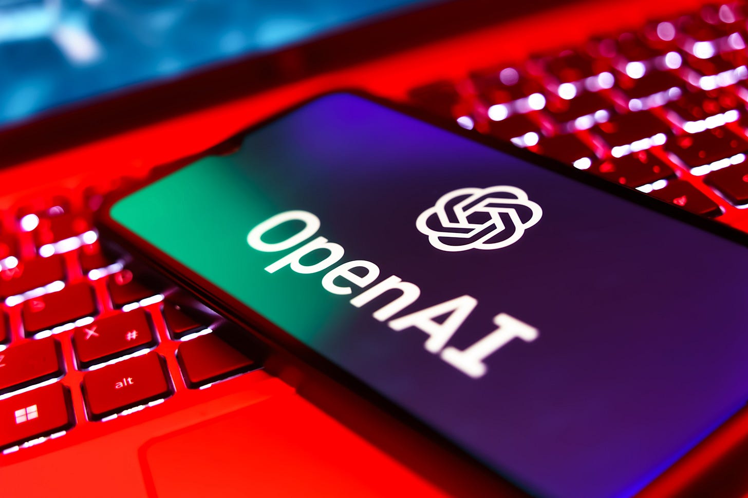 A smartphone displaying the OpenAI logo on a red-lit keyboard