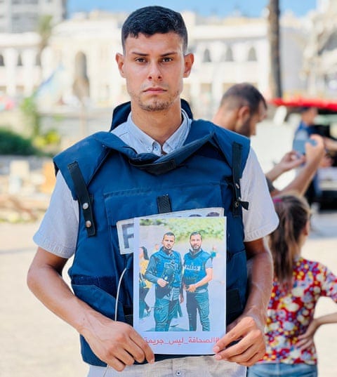 A young man in a blue press vest holds a picture of two other young men in blue press vests A young man in a blue press vest holds a picture of two other young men in blue press vests