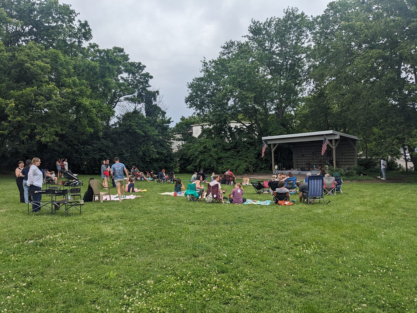 A mostly empty field with a few concertgoers near a stage