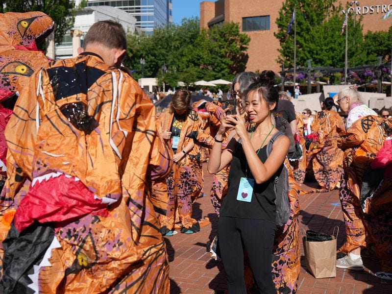 woman in normal clothes takes a photo of a person in an inflatable dinosaur costume