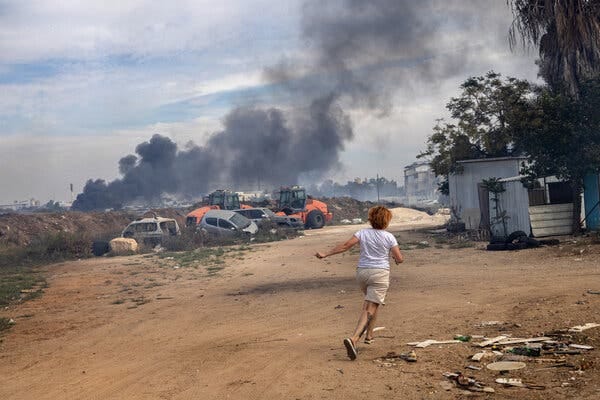 A woman running for shelter as smoke rises in the background.