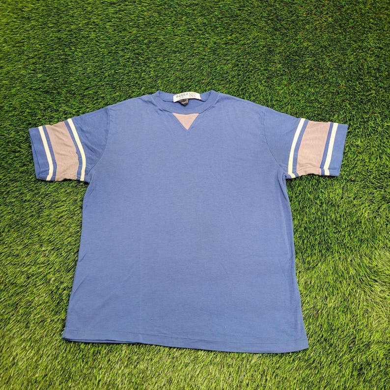 May include: A blue short-sleeved t-shirt with white and gray stripes on the sleeves. The shirt has a v-neck and a small white tag with the text 'ASICS' on the front.
