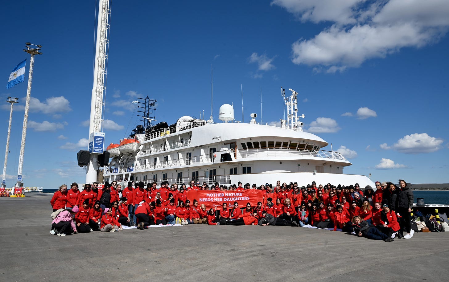 Group of women in red expedition gear gathered in front of a research vessel during the Homeward Bound Antarctica voyage, representing global collaboration in science and leadership