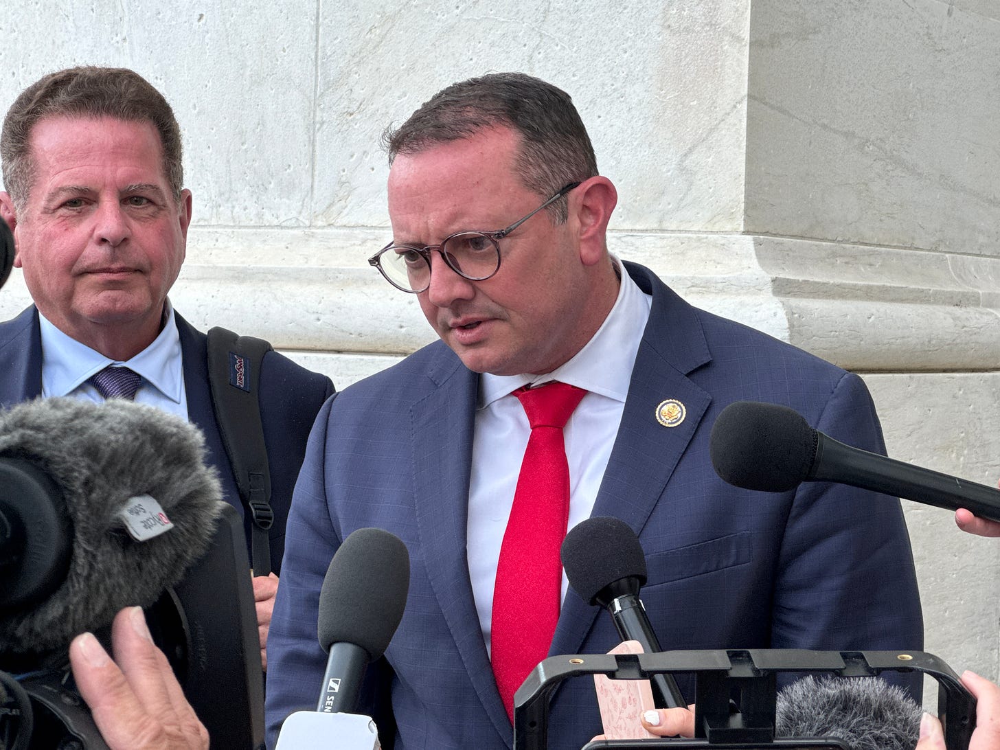 A politician in a suit answers reporters questions outside the US Capitol 