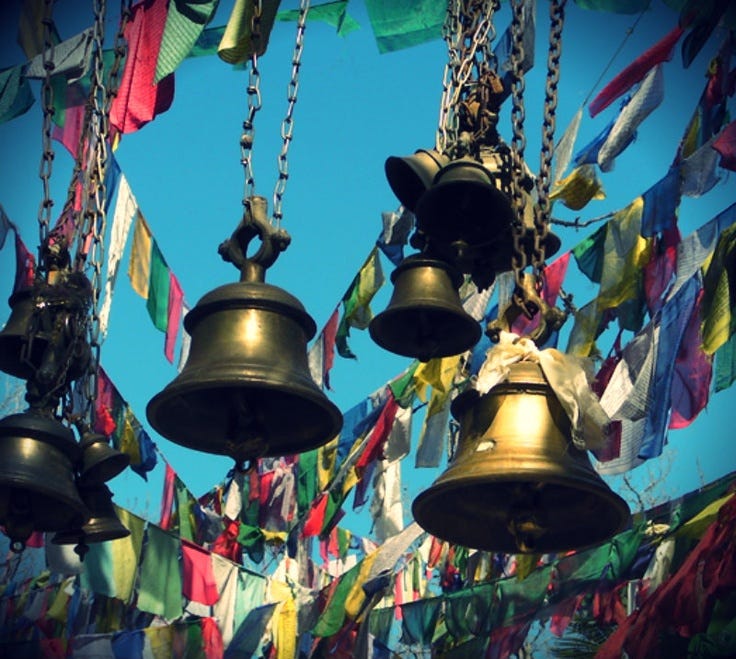 This may contain: several bells hanging from the ceiling with flags in the back ground and blue sky behind them