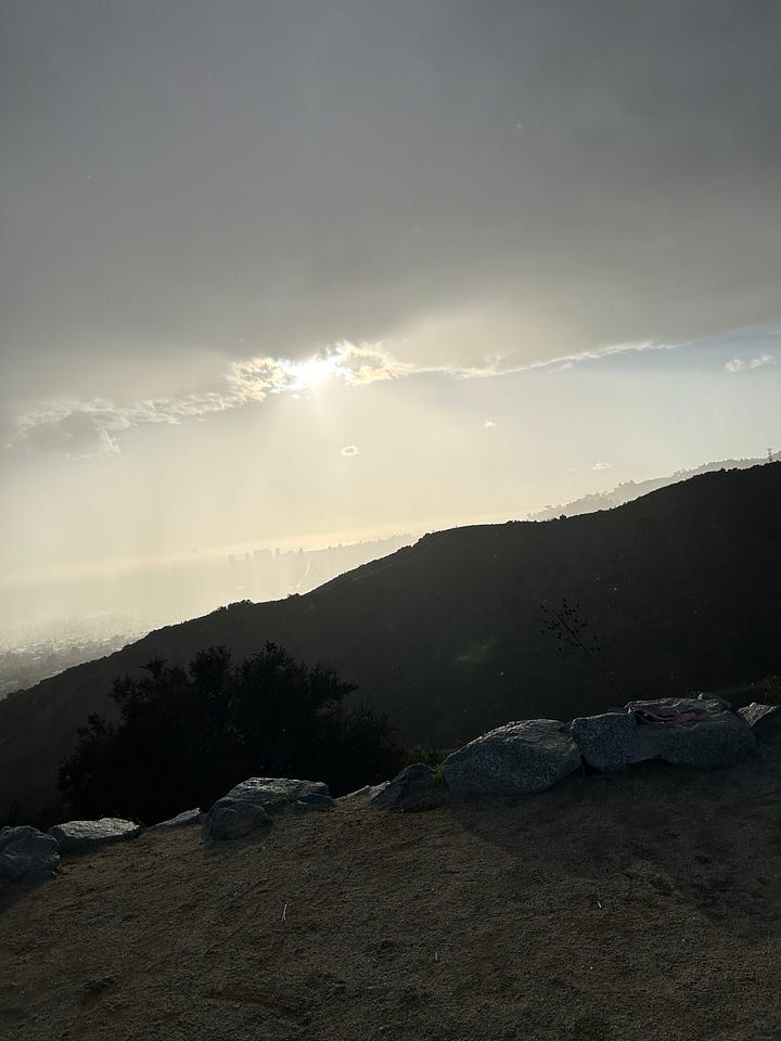 A downpour of rain just beyond the other ridge of the canyon, completely blocking the views from the hike; two photos of the views along the path up with dark rain clouds, and the paved path along the opposite ridge.