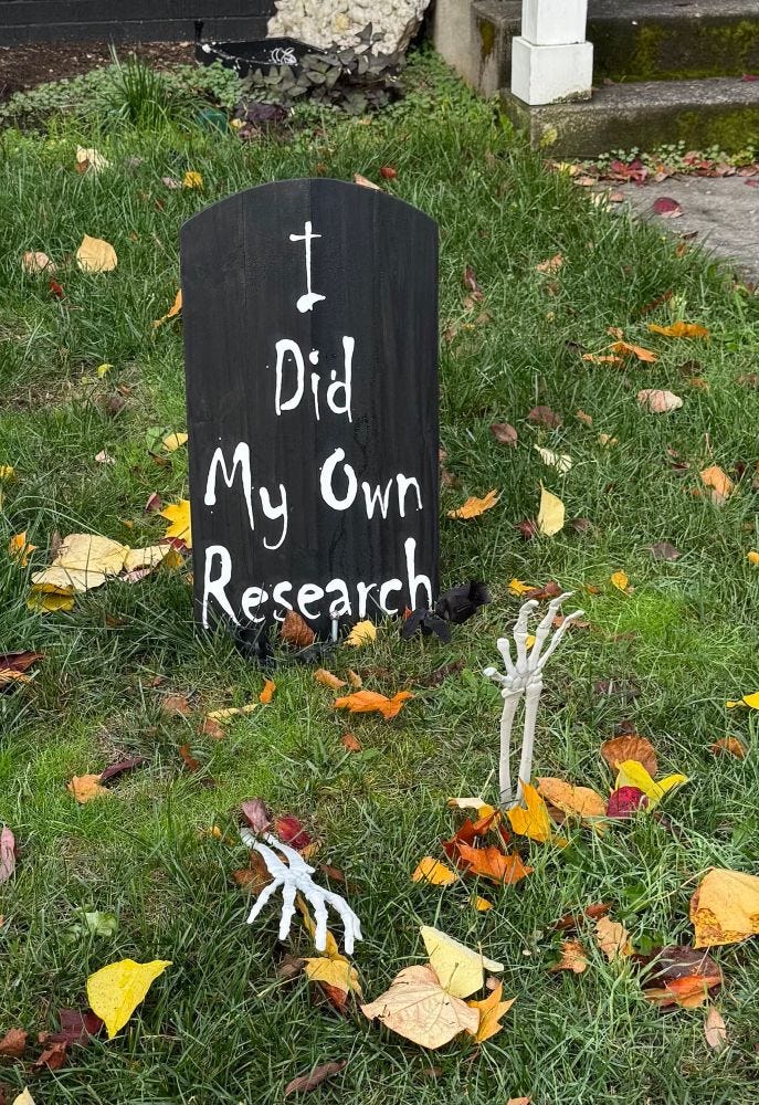 Halloween gravestone reading “I Did My Own Research” in a yard with two skeleton arms sticking out of the grass.