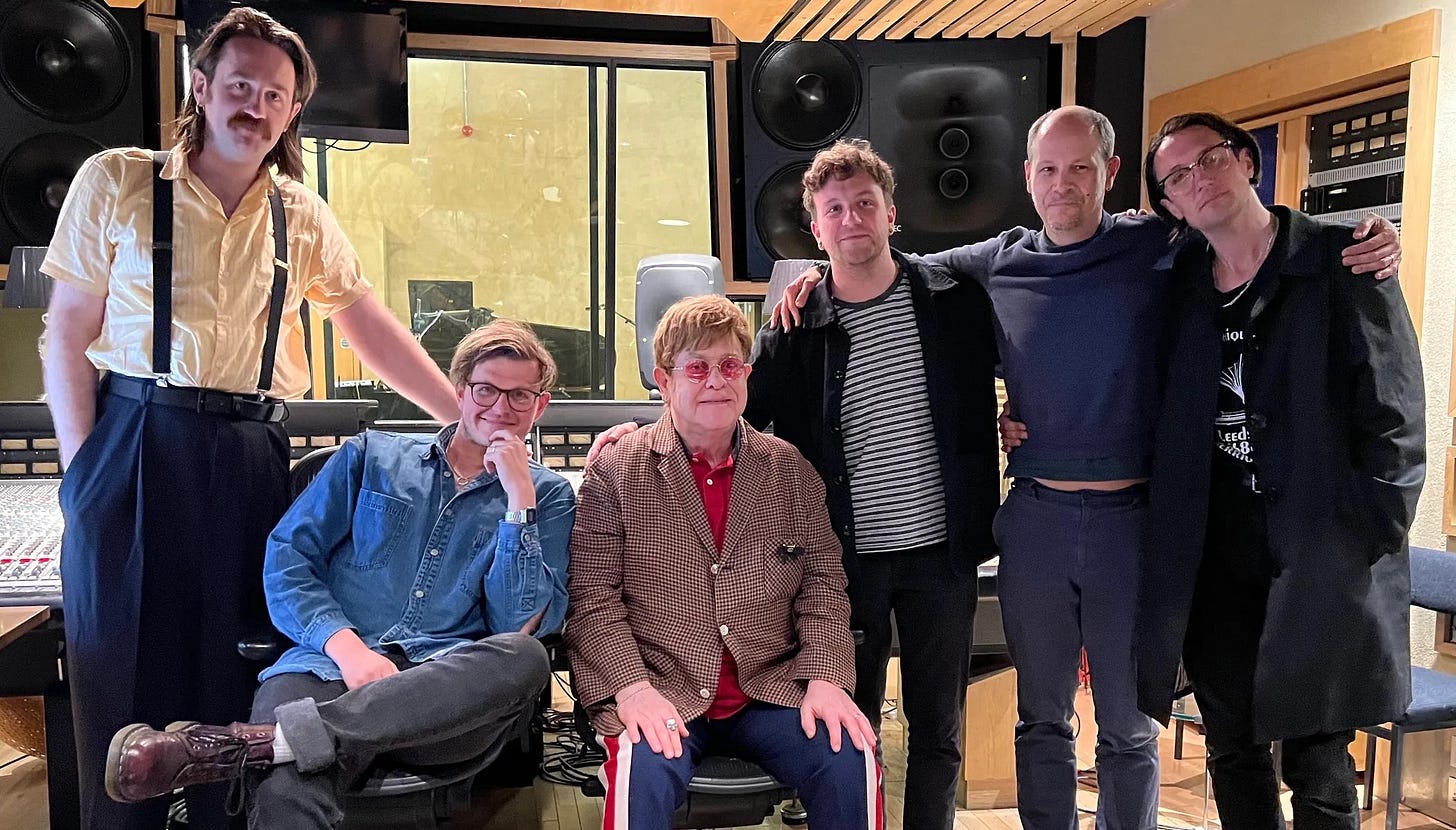 The members of Yard Act seated and standing inside a recording studio with Elton John and producer Ali Chant.